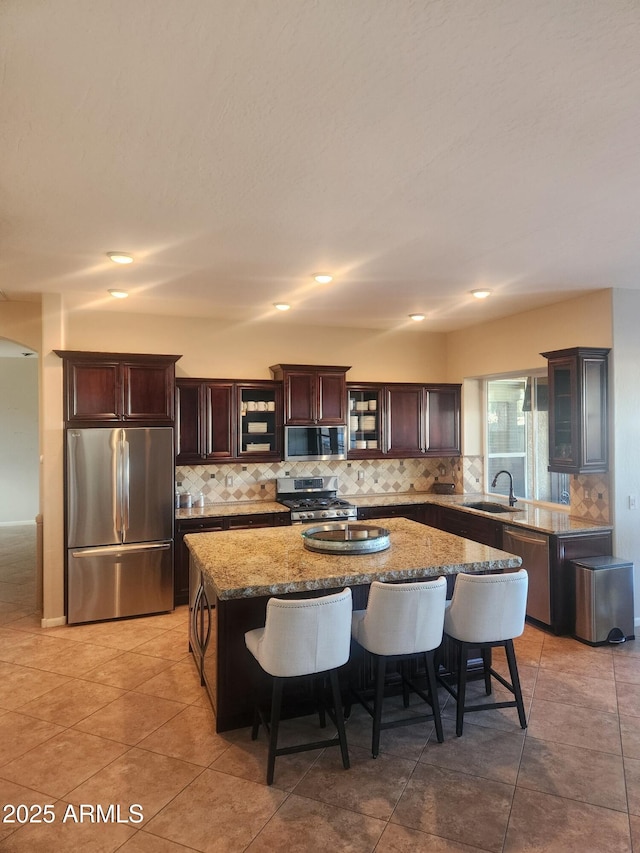 kitchen with a kitchen island, sink, a kitchen breakfast bar, light stone counters, and stainless steel appliances