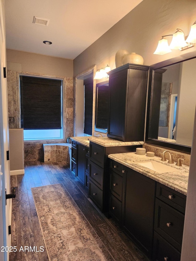 bathroom featuring hardwood / wood-style flooring, vanity, and tiled bath