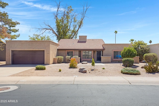 pueblo-style home with stucco siding, a tile roof, concrete driveway, an attached garage, and a chimney