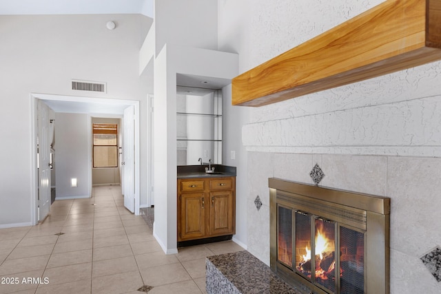 bar featuring visible vents, a tile fireplace, a high ceiling, light tile patterned flooring, and a sink