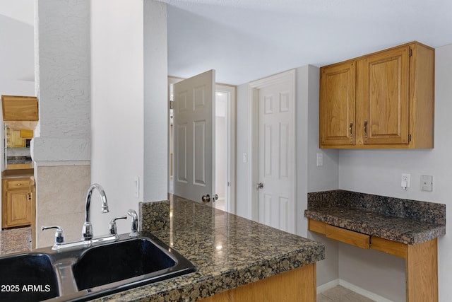 kitchen with a sink, baseboards, brown cabinets, and dark countertops