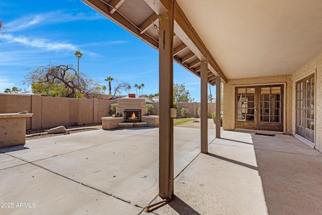 view of patio / terrace featuring french doors, a warm lit fireplace, and a fenced backyard