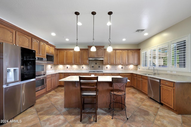 kitchen with brown cabinetry, visible vents, appliances with stainless steel finishes, a center island, and a sink