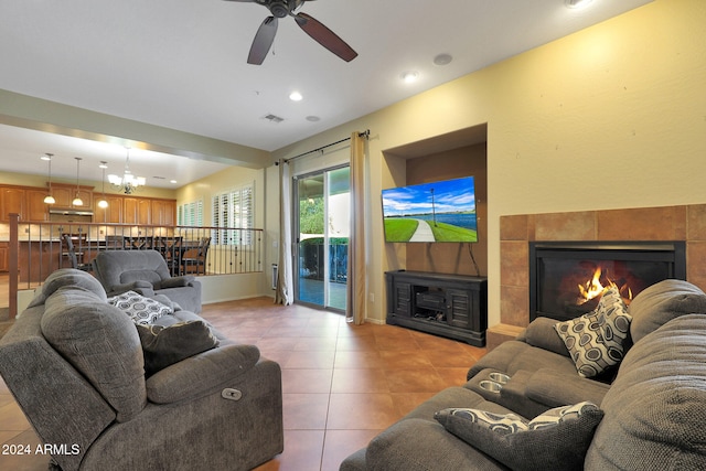 tiled living room with a fireplace and ceiling fan with notable chandelier