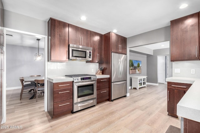 kitchen featuring hanging light fixtures, tasteful backsplash, appliances with stainless steel finishes, and light hardwood / wood-style floors