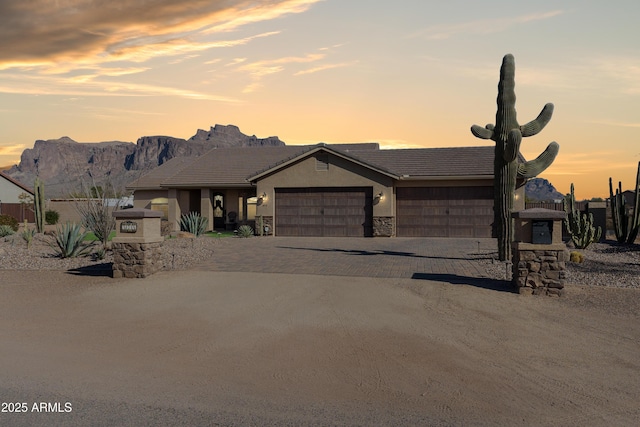 view of front of property featuring stucco siding, decorative driveway, stone siding, a mountain view, and an attached garage