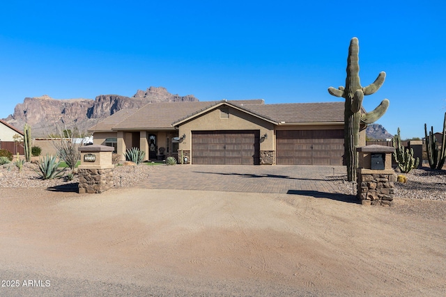 view of front of house featuring a mountain view, stucco siding, decorative driveway, stone siding, and an attached garage