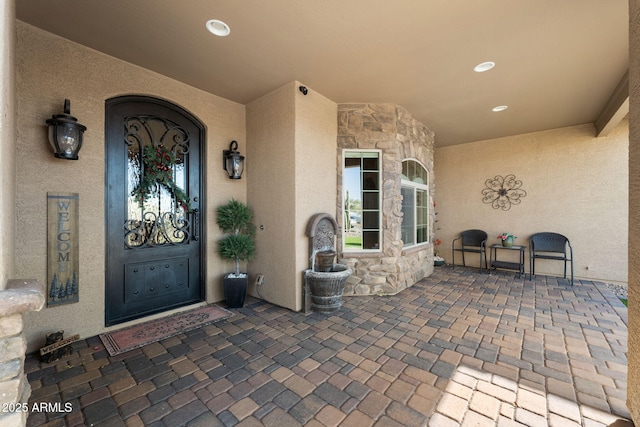 doorway to property featuring stucco siding, stone siding, and a patio