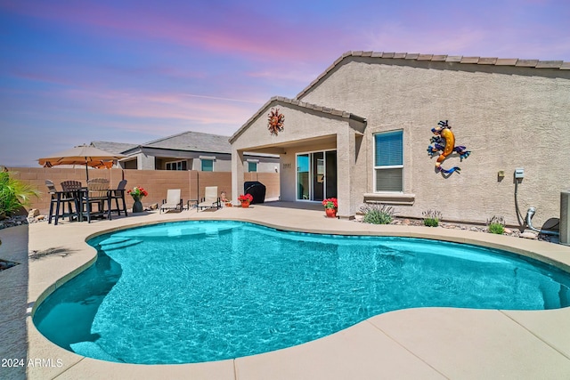 pool at dusk featuring a patio