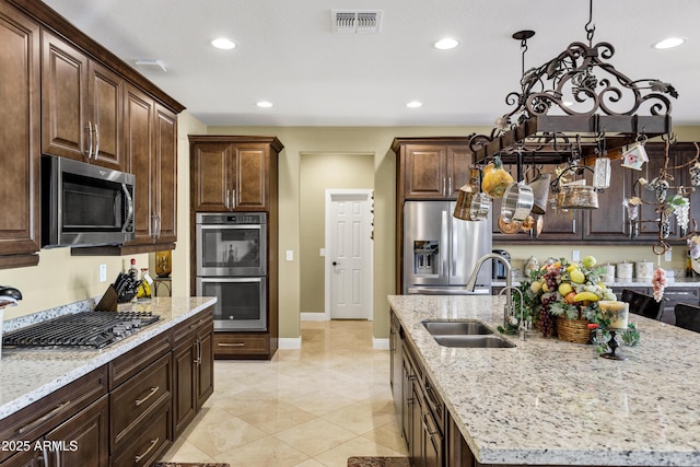 kitchen featuring an island with sink, appliances with stainless steel finishes, light stone countertops, and sink