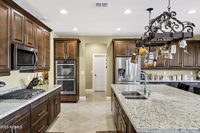 kitchen with stainless steel appliances, an island with sink, light stone countertops, and sink