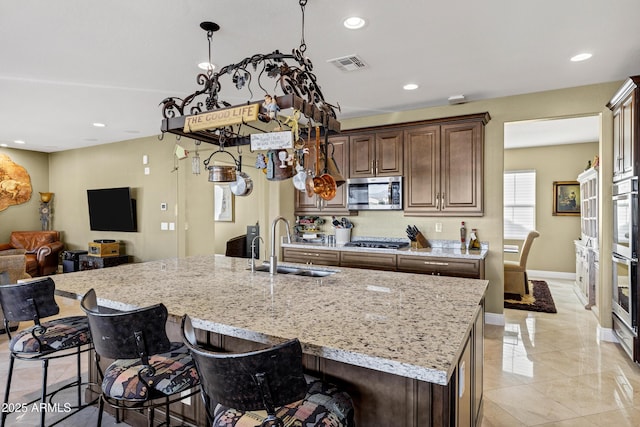 kitchen featuring sink, a kitchen breakfast bar, an island with sink, stainless steel appliances, and light stone countertops