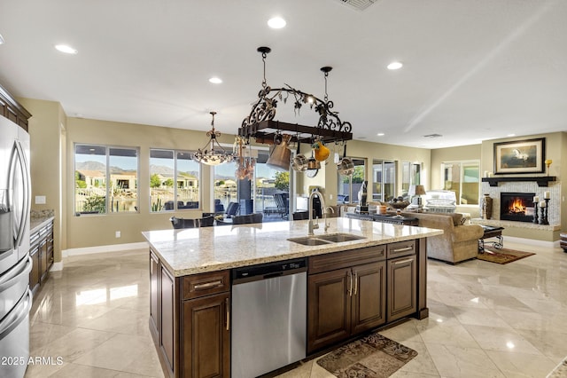 kitchen with sink, light stone counters, hanging light fixtures, appliances with stainless steel finishes, and a kitchen island with sink