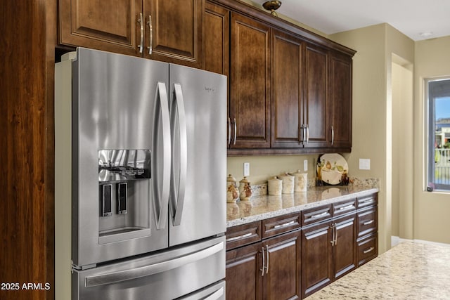 kitchen featuring dark brown cabinets, light stone counters, and stainless steel fridge with ice dispenser