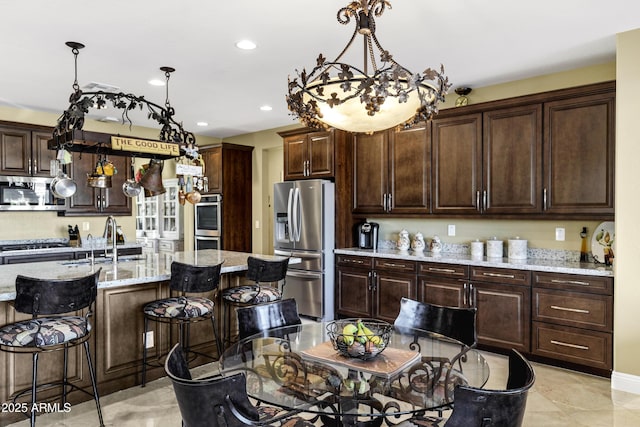 kitchen featuring pendant lighting, dark brown cabinetry, appliances with stainless steel finishes, and an island with sink