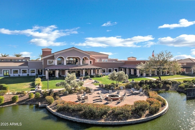 rear view of house featuring a patio, a water view, a lawn, and a fire pit