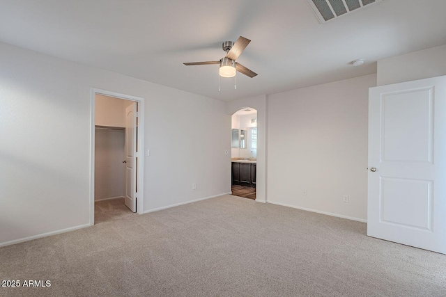 unfurnished bedroom featuring visible vents, carpet floors, baseboards, arched walkways, and a spacious closet