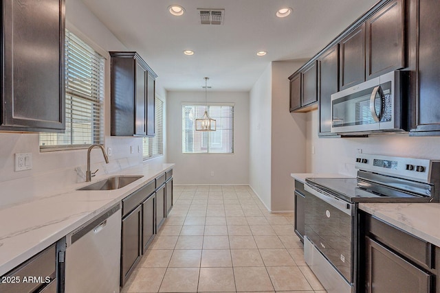 kitchen with visible vents, dark brown cabinetry, light stone counters, appliances with stainless steel finishes, and a sink