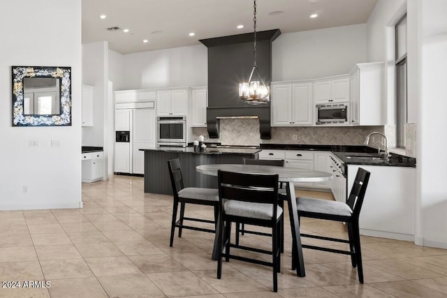 kitchen with sink, built in appliances, decorative light fixtures, white cabinets, and a high ceiling