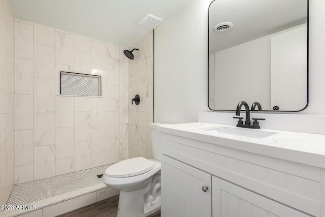 bathroom featuring tiled shower, hardwood / wood-style floors, vanity, and toilet