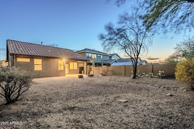 back of property at dusk featuring stucco siding, a tiled roof, and fence