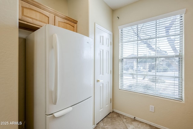 kitchen featuring light tile patterned floors, light brown cabinets, freestanding refrigerator, and baseboards