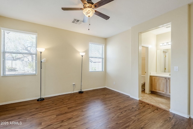 unfurnished bedroom with wood finished floors, visible vents, baseboards, ceiling fan, and ensuite bathroom