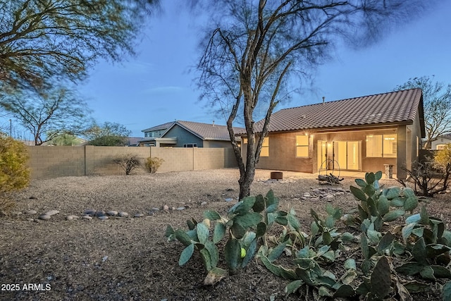 rear view of property with stucco siding, a tile roof, and a fenced backyard