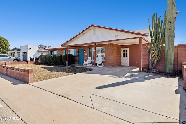 view of front of house with an attached carport, concrete driveway, fence, and brick siding