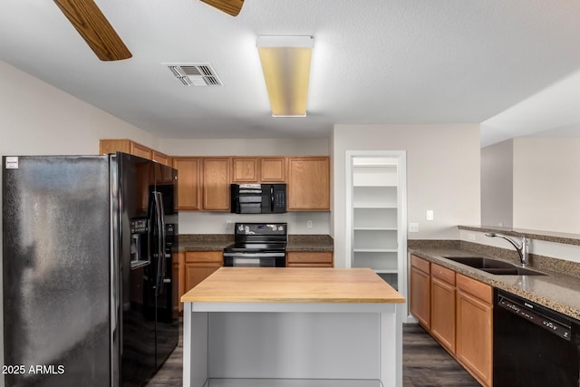 kitchen featuring visible vents, butcher block counters, a sink, dark wood finished floors, and black appliances