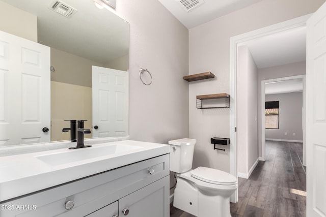 bathroom with vanity, toilet, wood finished floors, and visible vents