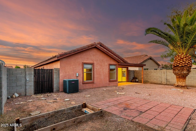 rear view of house with stucco siding, a fenced backyard, a gate, central AC unit, and a patio
