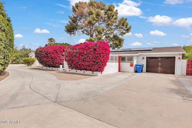 6747 N 12th St, Phoenix, AZ 85014 - view of front facade with fence, roof mounted solar panels, an attached garage, stucco siding, and driveway