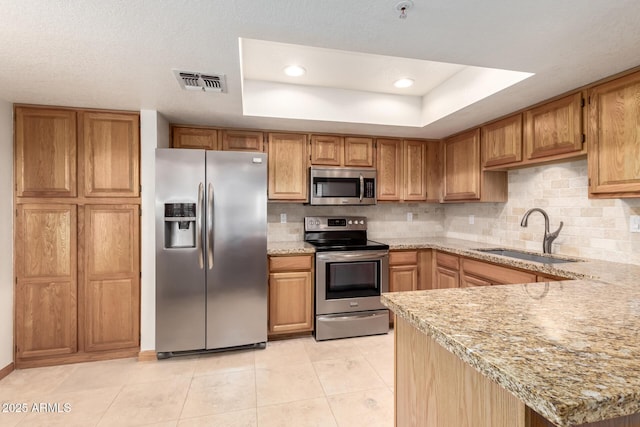 kitchen with appliances with stainless steel finishes, a raised ceiling, visible vents, and a sink