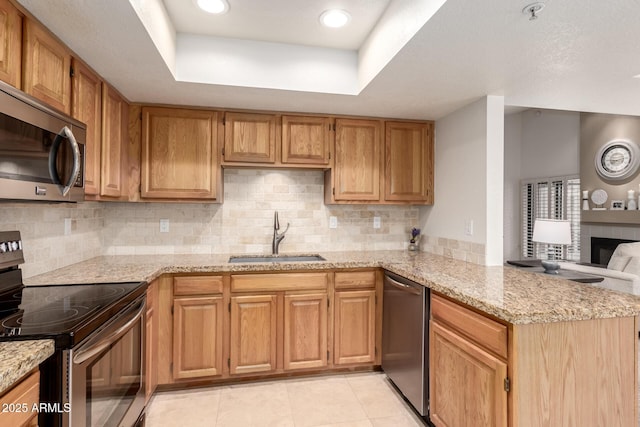 kitchen with a peninsula, a tray ceiling, stainless steel appliances, and a sink