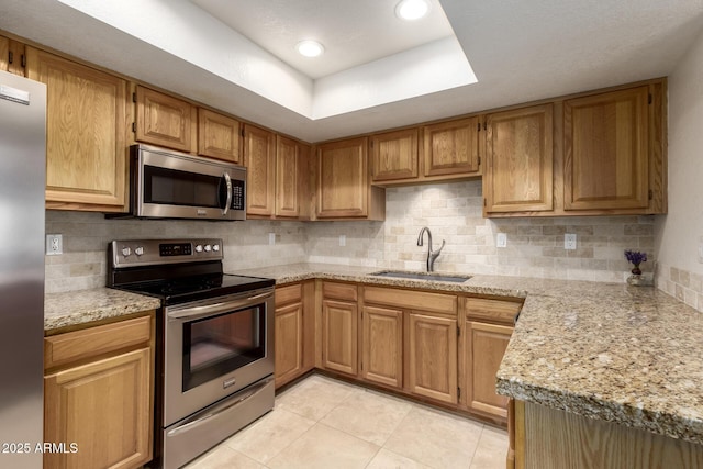 kitchen featuring light tile patterned floors, stainless steel appliances, a sink, a tray ceiling, and tasteful backsplash