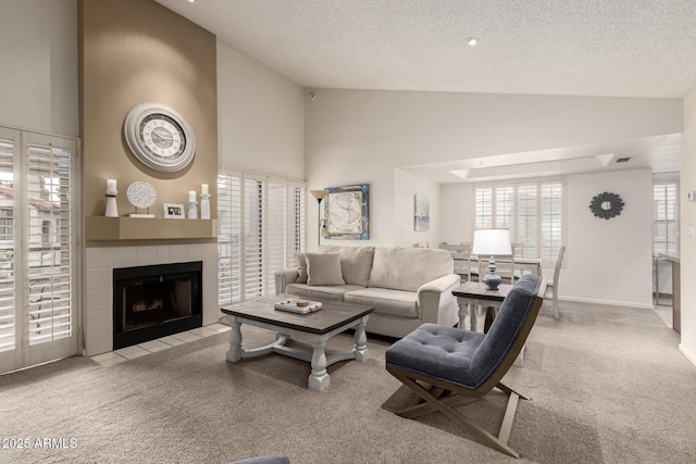 living area with a textured ceiling, a tiled fireplace, high vaulted ceiling, and carpet flooring