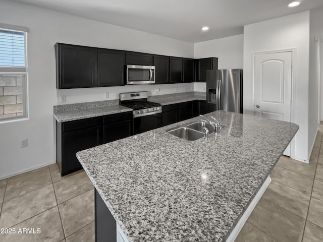 kitchen featuring stainless steel appliances, light stone counters, and a center island with sink