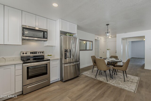 16421 N 34th Ave, Phoenix, AZ 85053 - kitchen featuring appliances with stainless steel finishes, white cabinets, light wood-style flooring, hanging light fixtures, and a textured ceiling