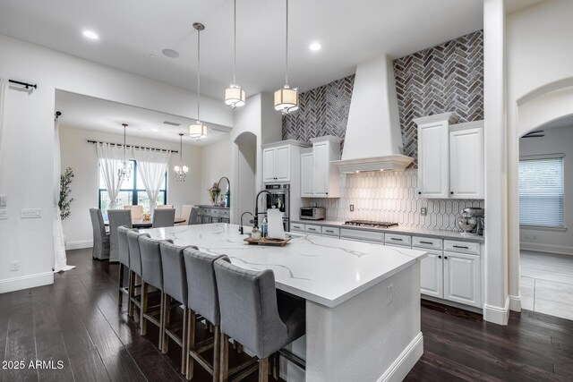 9527 W Whitehorn Way, Peoria, AZ 85383 - kitchen featuring custom range hood, arched walkways, a center island with sink, appliances with stainless steel finishes, and a breakfast bar area