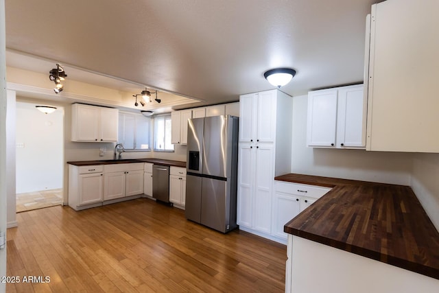 kitchen with a sink, appliances with stainless steel finishes, white cabinets, and light wood finished floors