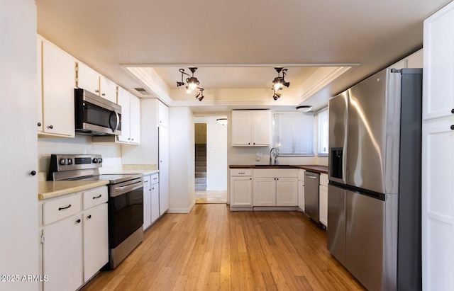 kitchen featuring a sink, light wood-style floors, appliances with stainless steel finishes, white cabinets, and a raised ceiling