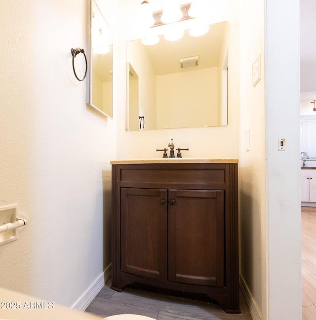 bathroom with visible vents, vanity, baseboards, and wood finished floors