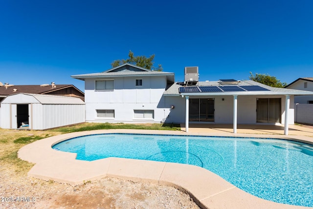 outdoor pool featuring fence, central air condition unit, a patio area, a storage unit, and an outbuilding