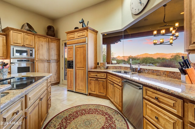 kitchen with built in appliances, sink, a chandelier, light stone countertops, and decorative light fixtures