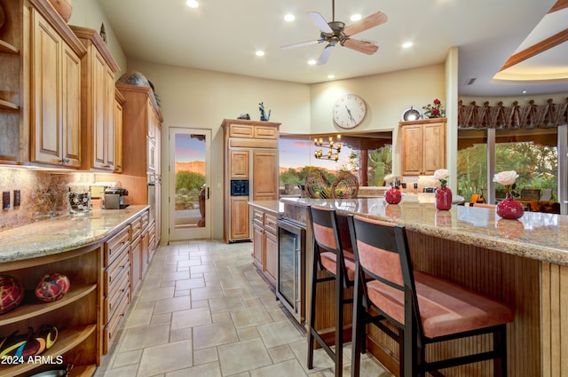 kitchen with tasteful backsplash, wine cooler, stainless steel oven, light stone countertops, and a breakfast bar area