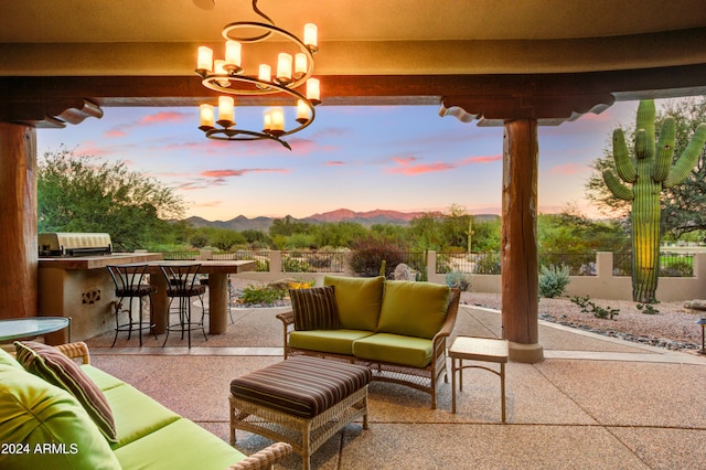 patio terrace at dusk with grilling area, exterior bar, exterior kitchen, a mountain view, and an outdoor hangout area