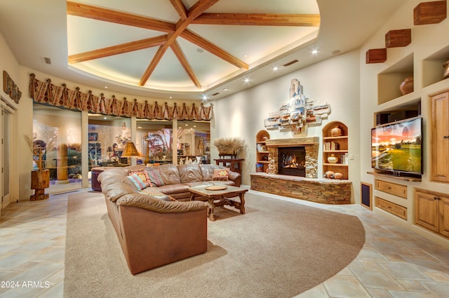 living room with built in shelves, beamed ceiling, a stone fireplace, and a towering ceiling