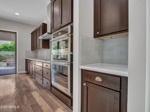 3809 E Lynx Pl, Chandler, AZ 85249 - kitchen with stainless steel double oven, dark brown cabinetry, decorative backsplash, dark wood-type flooring, and baseboards