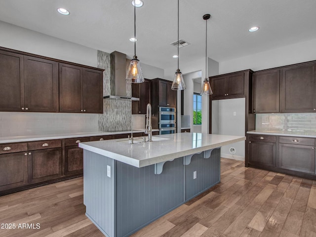 3809 E Lynx Pl, Chandler, AZ 85249 - kitchen featuring wall chimney exhaust hood, backsplash, light wood finished floors, dark brown cabinets, and stainless steel double oven